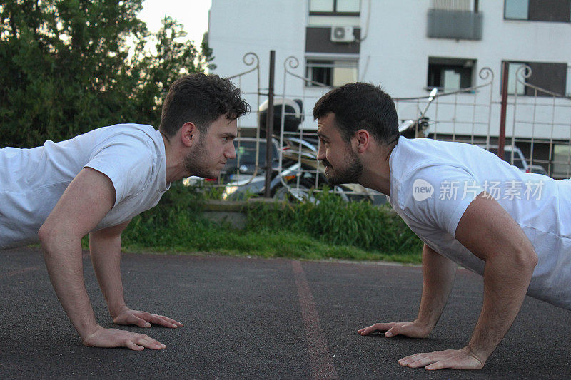 Two white men doing pushups together in a public park